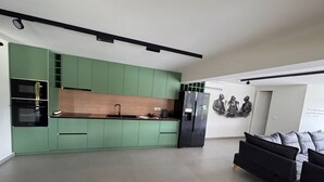 Une cuisine moderne avec des meubles de couleur verte, un réfrigérateur noir et un coin repas agrémenté d’un canapé noir.