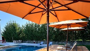Un espace aménagé au bord de la piscine, avec des chaises longues et des parasols, une terrasse en bois et une piscine.