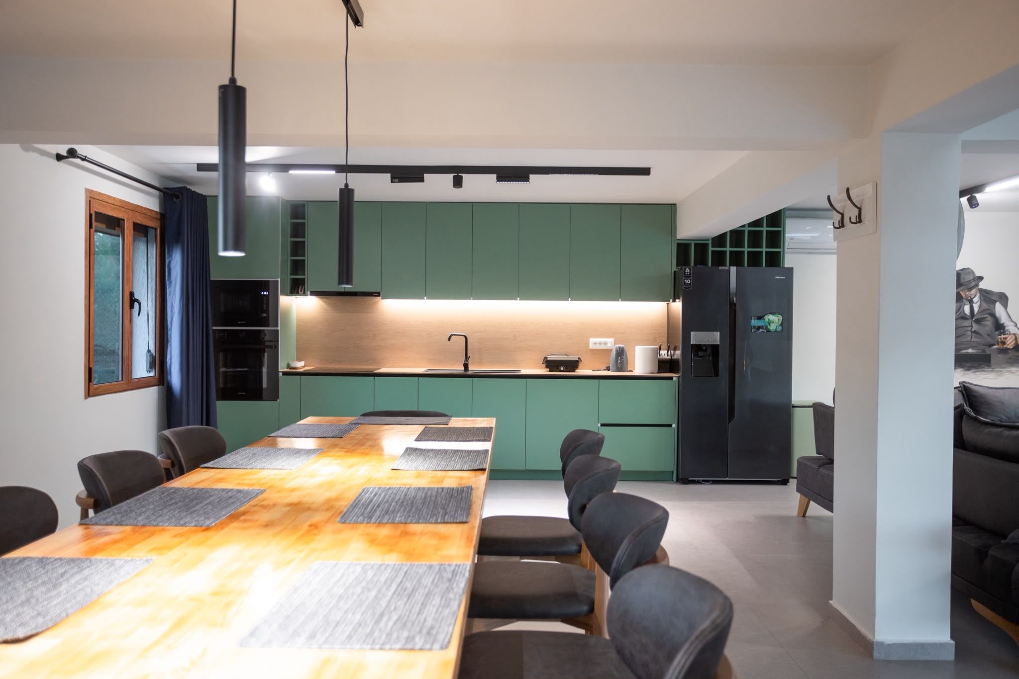 A modern kitchen with green cabinets, a black refrigerator, and a dining area with a wooden table and chairs.