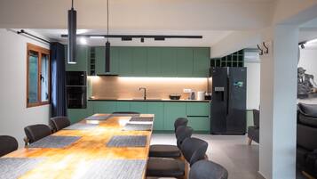 A modern kitchen with green cabinets, a black refrigerator, and a dining area with a wooden table and chairs.