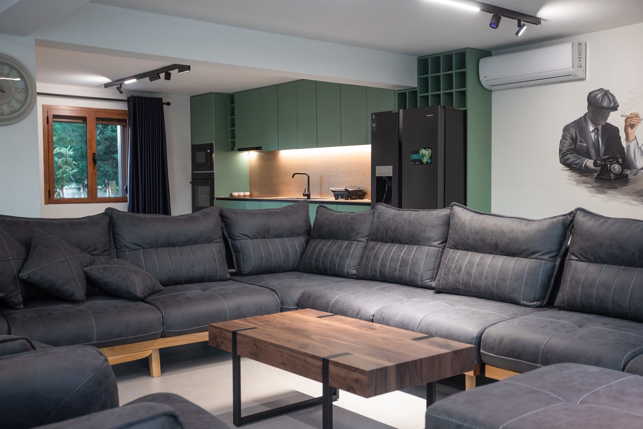 A modern living room with a sectional sofa, a wooden coffee table, and a kitchen area in the background.