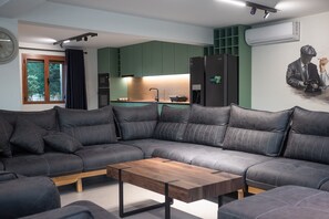Un salon moderne avec un canapé d’angle, une table basse en bois et un coin cuisine à l’arrière-plan.