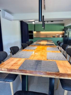 A conference room with a long table, black chairs, and a kitchen area in the background.