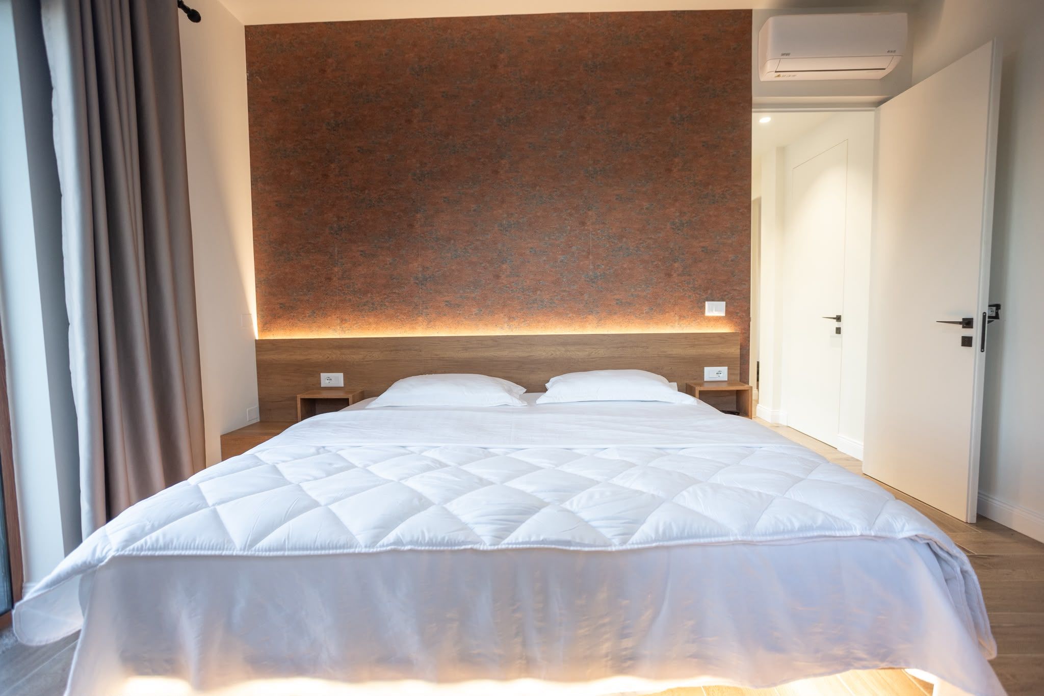 Een hotelkamer met een groot bed, een houten hoofdbord, nachtkastjes en een deur.