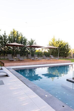 A swimming pool with lounge chairs and umbrellas, surrounded by trees.