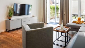 A modern living room with a flat-screen TV, a sofa, a coffee table, and a sliding glass door leading to an outdoor area. - Grömitz MeerNah No 4. sauna. Terrace. Close to the beach. (Grömitz)