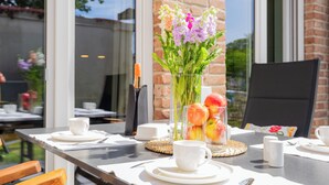 A dining table with white cups, saucers, and a vase with flowers and fruit. - Grömitz MeerNah No 4. sauna. Terrace. Close to the beach. (Grömitz)