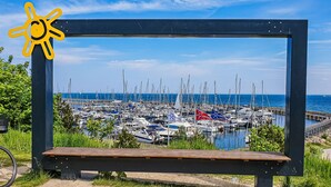A marina with numerous boats docked, a clear blue sky, and a wooden bench in the foreground. - Grömitz MeerNah No 4. sauna. Terrace. Close to the beach. (Grömitz)
