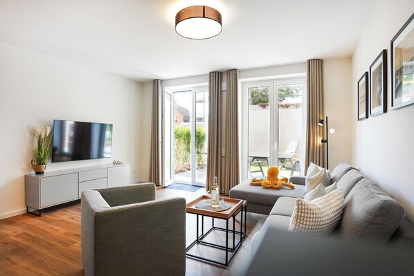 Een moderne woonkamer met een flatscreen televisie, een bank, een salontafel en een eethoek met een stoel.