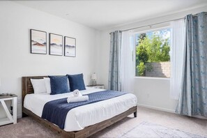 Une chambre à coucher avec un lit en bois, du linge de lit blanc, une table de chevet, une lampe et trois tableaux encadrés accrochés au mur.