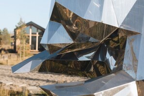 A geometric metal sculpture with a reflective surface, set against a natural landscape with a building in the background. - Yellowstone Peaks Hotel (Island Park)