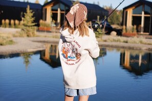 A person fishing by a calm body of water with wooden cabins in the background. - Yellowstone Peaks Hotel (Island Park)