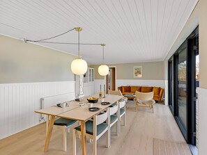A dining area with a table and chairs, a sofa, and a view through a glass door.
