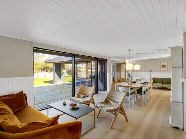 Un intérieur moderne comprenant un coin repas, un canapé et une vue dégagée grâce à de grandes portes vitrées.