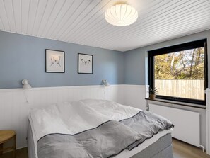 Une chambre à coucher comprenant un lit, deux lampes fixées au mur, une fenêtre donnant sur des arbres et un luminaire au plafond.