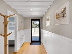 A hallway with a wooden floor, white walls, a black door, and framed artwork.