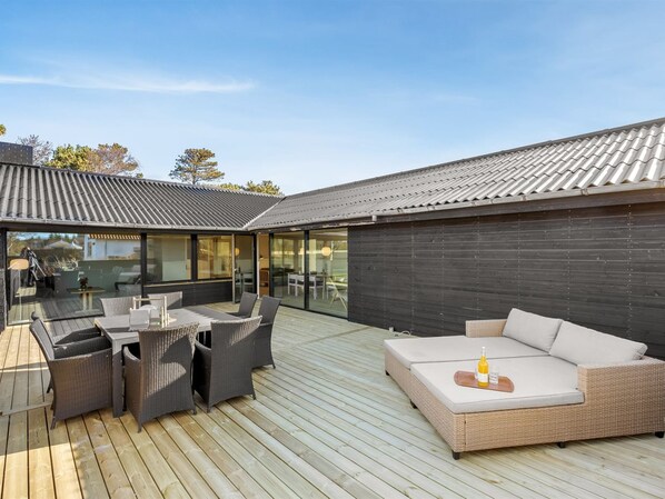 A modern outdoor patio with a dining area, a sofa, and a glass-enclosed space.