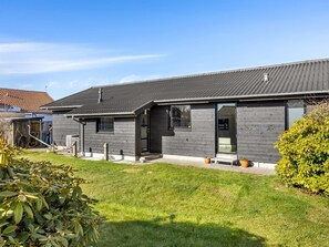 Une maison moderne à deux étages, avec une façade de couleur gris foncé, un toit en pente et une pelouse bien entretenue.
