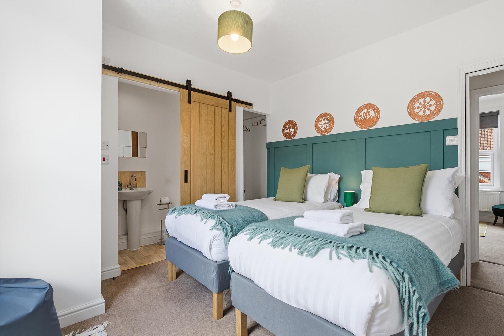 A hotel room with two beds, a wooden door, a bathroom, and decorative wall plates.