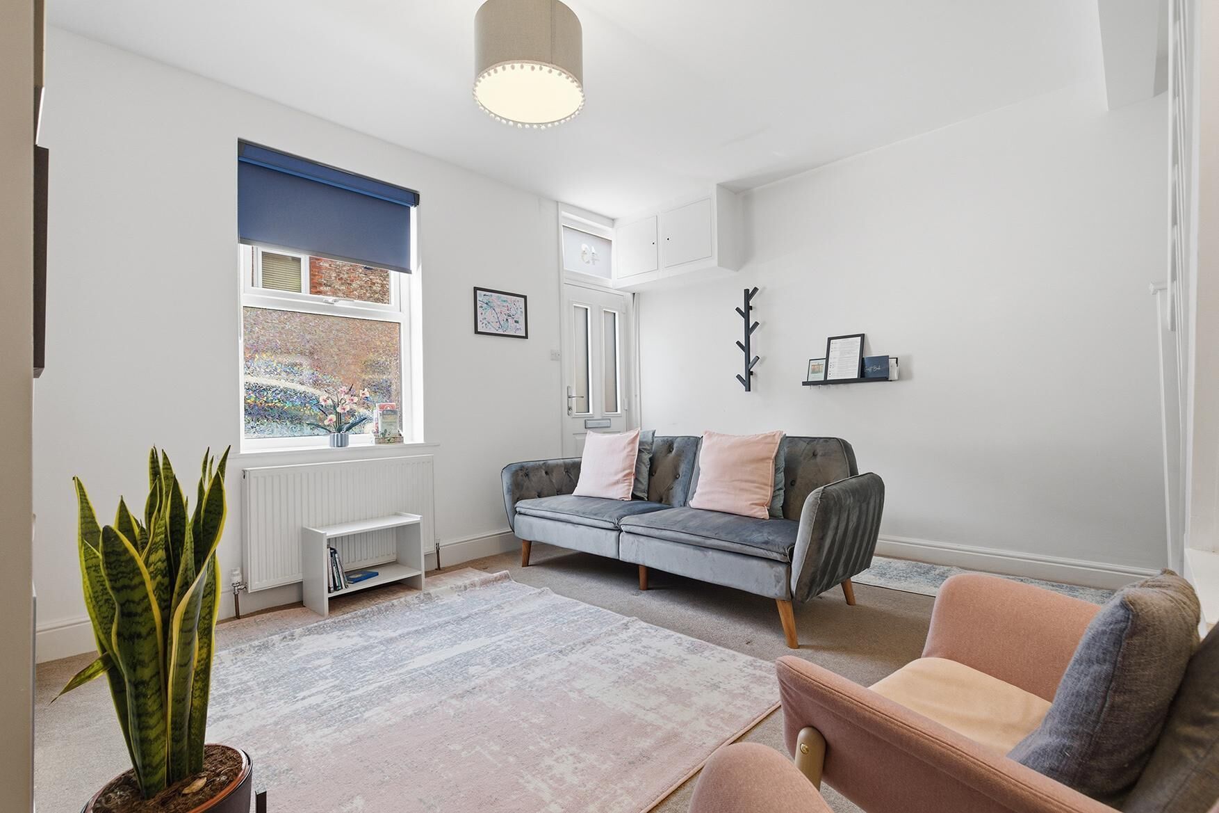 A modern living room with a sofa, a chair, a radiator, a window with blinds, and a potted plant.