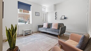 Una sala de estar moderna con un sofá, una silla, un radiador, una ventana con persianas y una planta en maceta.