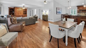 Amplia sala de estar con piso de madera, comedor con sillas blancas, sofá y aparador de madera.