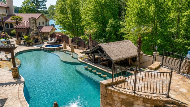 Una piscina con un deck de piedra, un pabellón y una estructura de techo de paja.