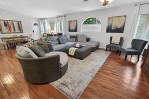 A living room with a sectional sofa, a small round table, and a dining table.