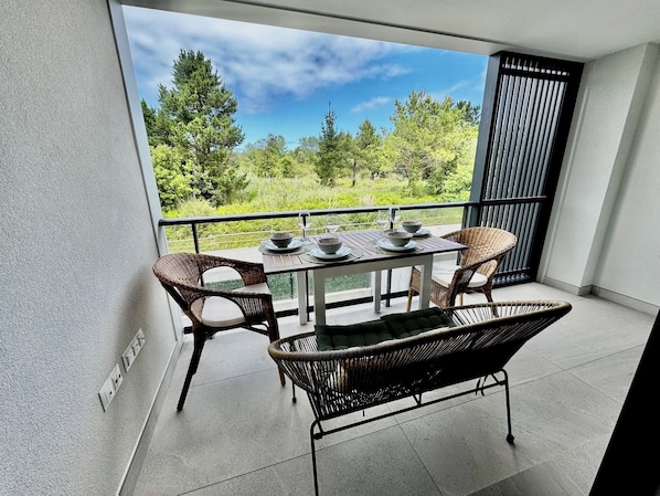 Ein Balkon mit Tisch für zwei Personen, Korbstühlen und Blick auf einen Wald.