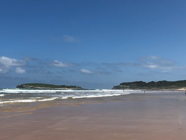 A beach with waves, a clear sky, and distant hills.