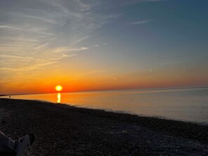 Een zonsondergang boven een kalm wateroppervlak met een kiezelstrand.