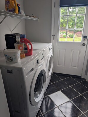 Een wasserette met een wasmachine, wasmiddel en een plank met schoonmaakmiddelen.