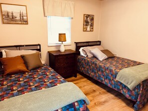 A bedroom with two beds, a nightstand, a lamp, and artwork on the walls.
