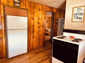 Una cocina con paneles de madera, un refrigerador, una estufa y una cama al fondo.