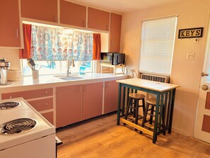 A compact kitchen with a stove, sink, and a small bar stool.