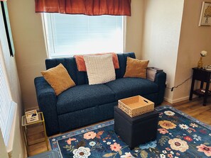 A living room with a dark blue sofa, a floral rug, and a small wooden table.