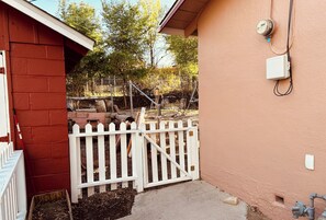A fenced outdoor area with a red building, a white picket fence, and a utility box on the wall.