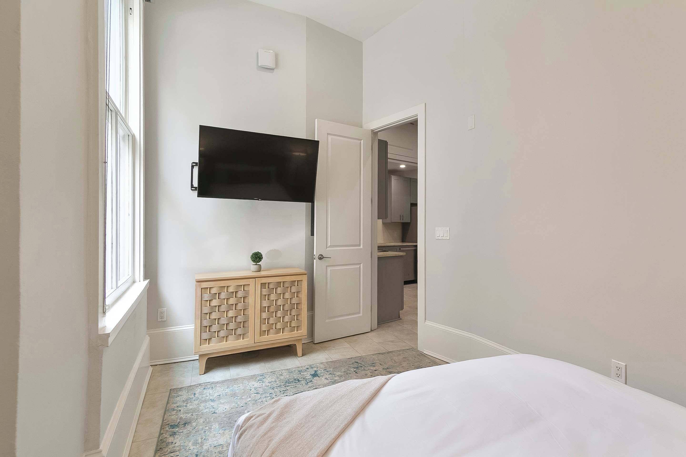 Ein Schlafzimmer mit einem Bett, einem an der Wand montierten Fernseher, einem Holzschrank und einer Tür zu einem Badezimmer.