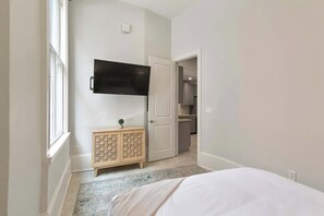 A bedroom with a bed, a TV mounted on the wall, a wooden cabinet, and a door leading to a bathroom.