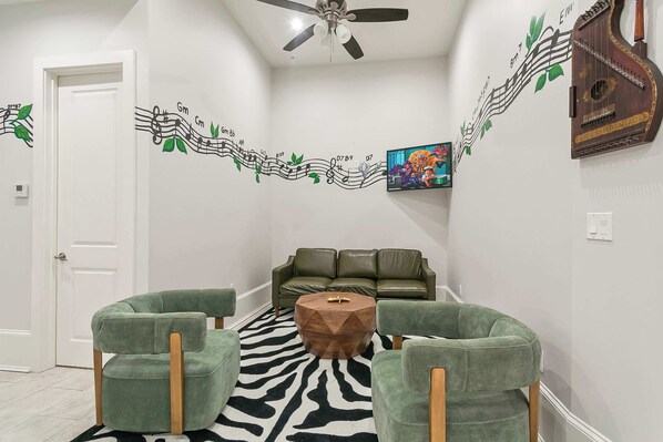 A room with a zebra-patterned rug, green upholstered chairs, a round wooden coffee table, a green sofa, and a wall with a musical notes mural.