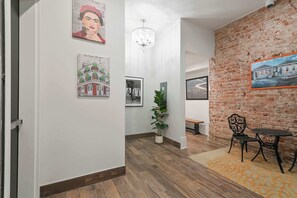 A hallway with a brick wall, wooden flooring, a chandelier, and framed artwork.