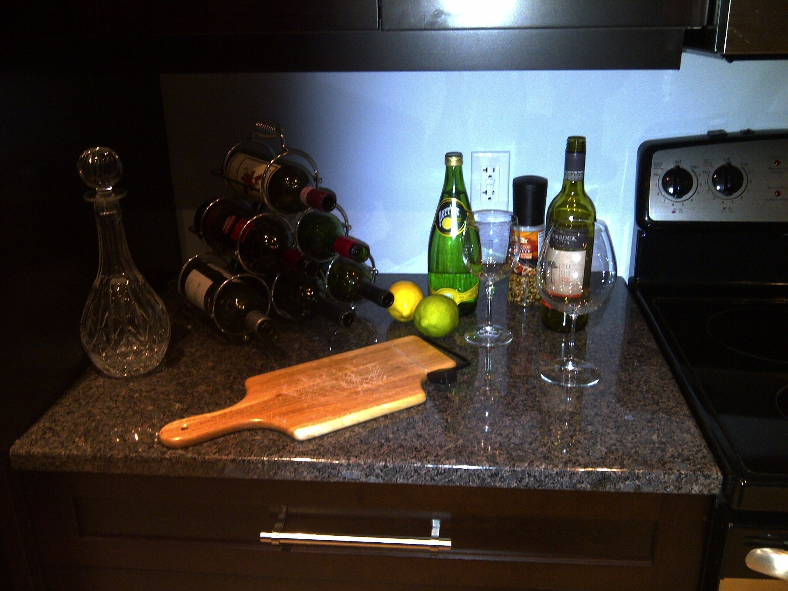 Un piano di lavoro in cucina con bottiglie di vino, bicchieri e tagliere.