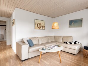 Ein modernes Wohnzimmer mit einem beigen Ecksofa, einem runden Couchtisch und einer hängenden Pendelleuchte.