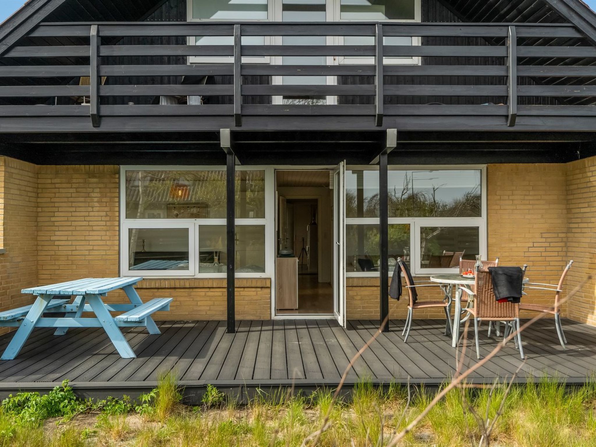 En træterrasse med et bord og stole, en skydedør i glas og en murstensvæg.