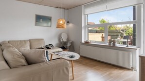 Un salon moderne avec un canapé, une table, une chaise, un luminaire suspendu et une fenêtre donnant sur l’extérieur.