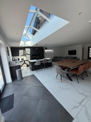 A modern kitchen with a skylight, a dining area with a large table and chairs, and a living area with a sofa and TV. - Carbis Bay Retreat (Carbis Bay)