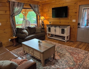 Ein gemütliches Blockhaus-Interieur mit einer Couch, einem Couchtisch, einem Fernseher und einem Schrank.