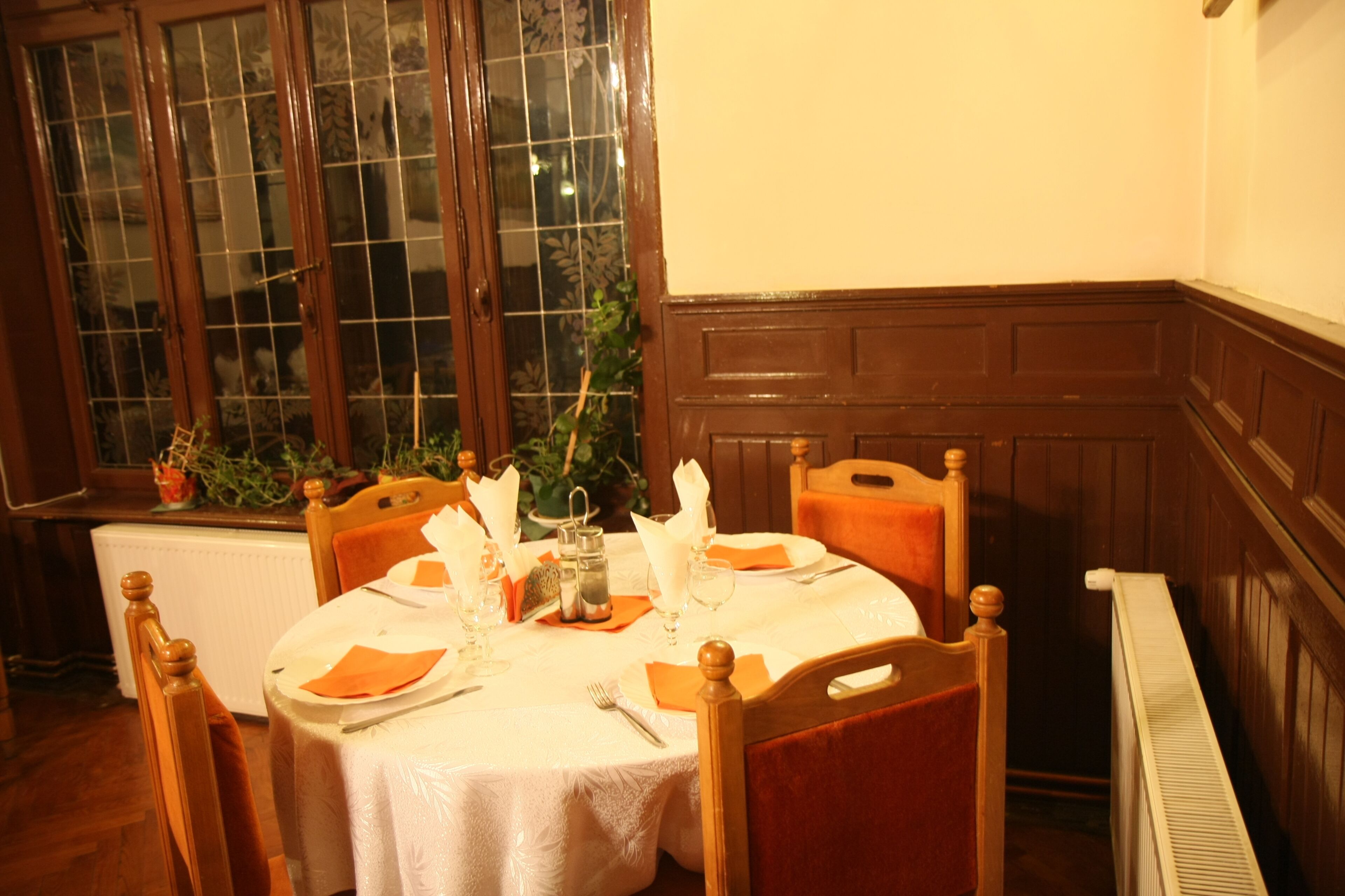 A dining room with a round table set for four, wooden chairs, a window with decorative glass panes, and a radiator.