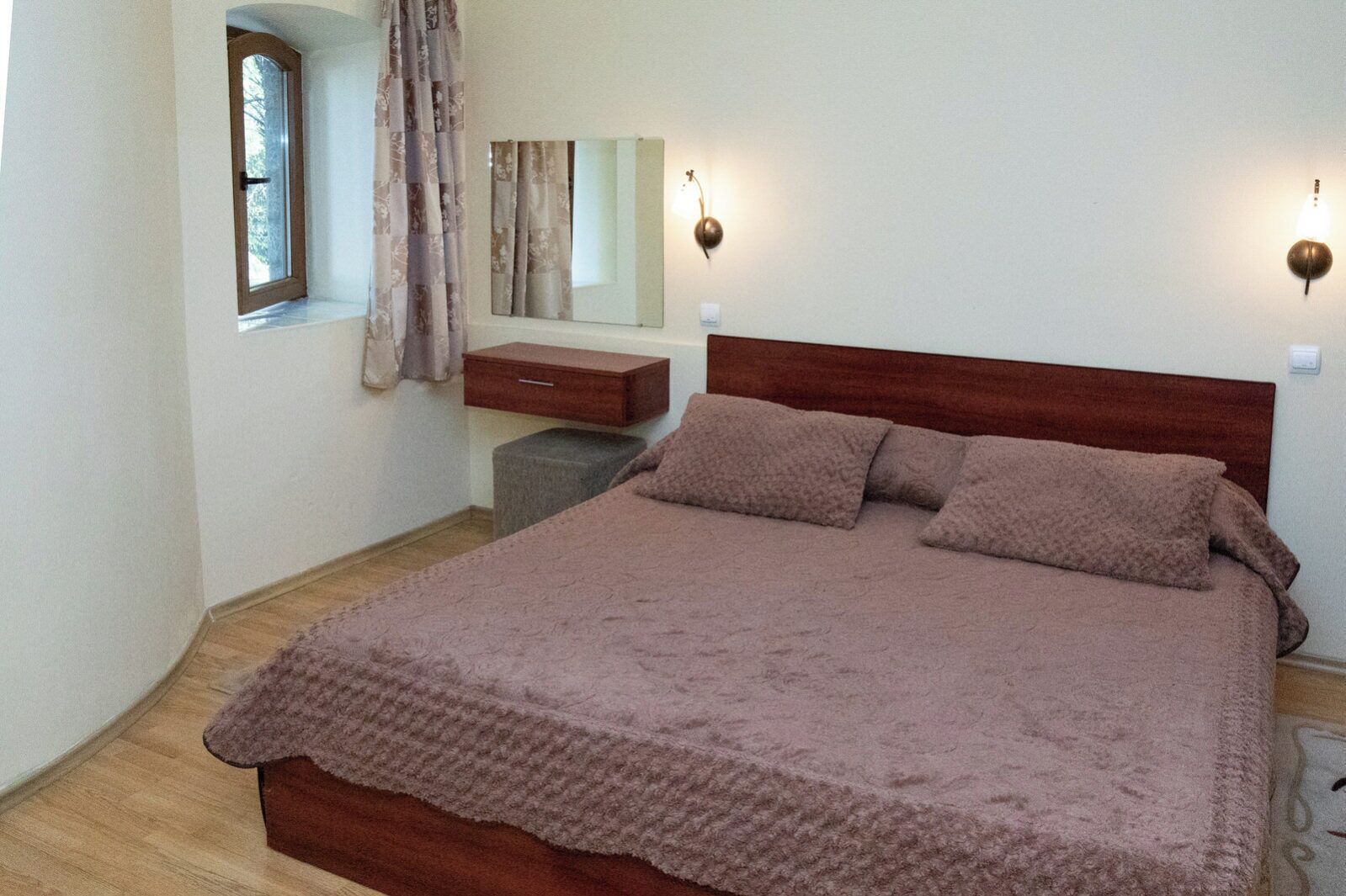 Camera da letto con un letto, un comodino, uno specchio, una finestra con tende e luci a parete.