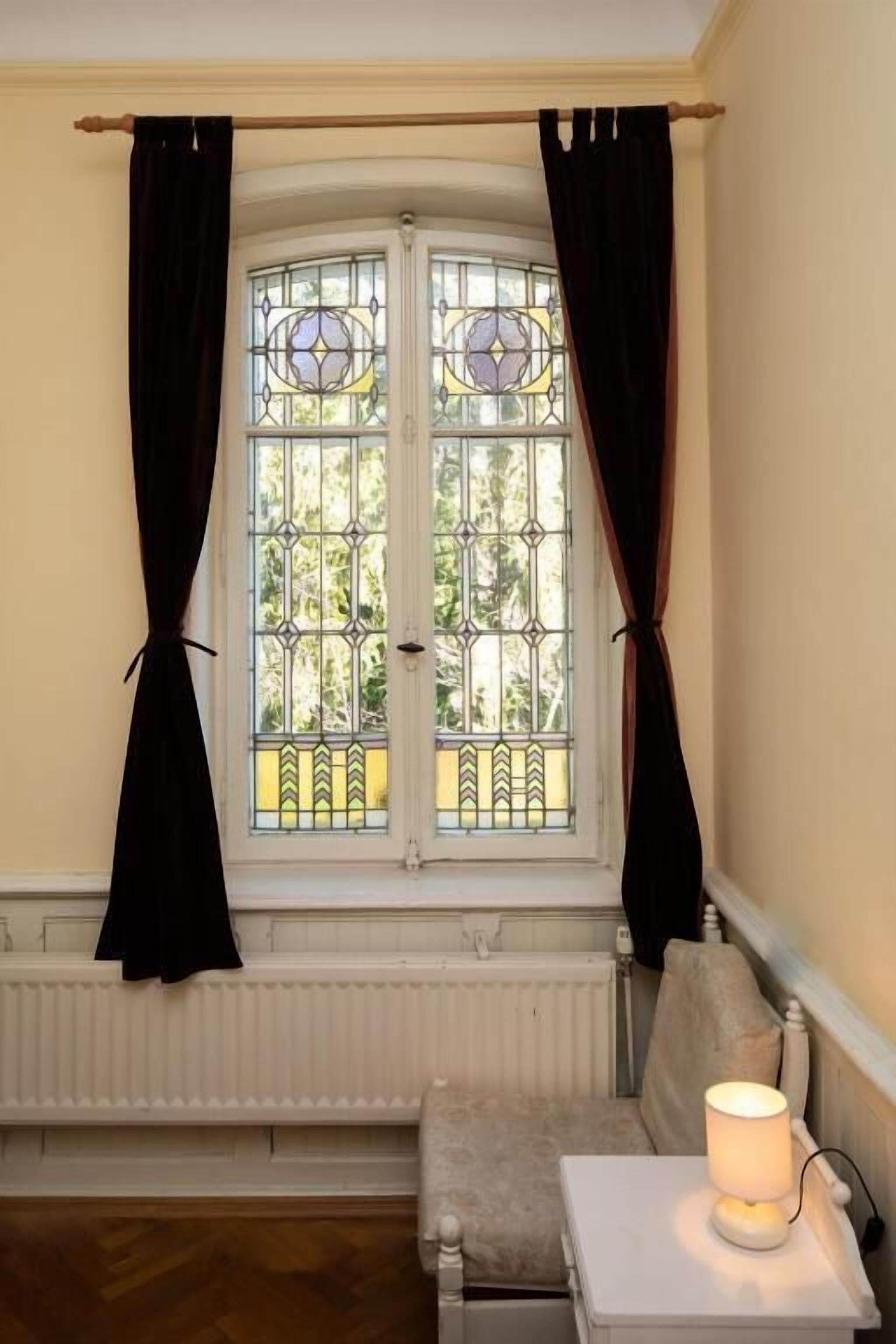 A room with a window, a radiator, a bench, and a bedside table with a lamp.